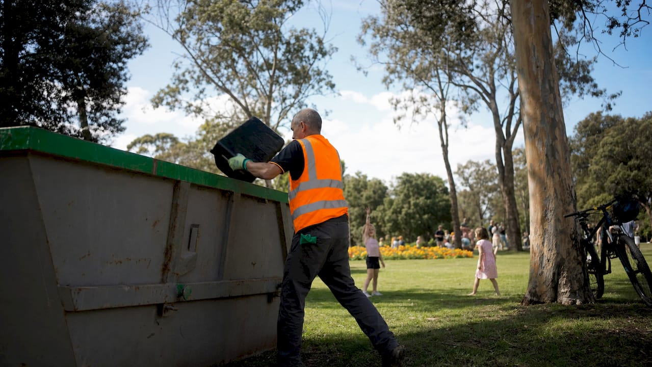 Man placing waste into skip bin outdoors
