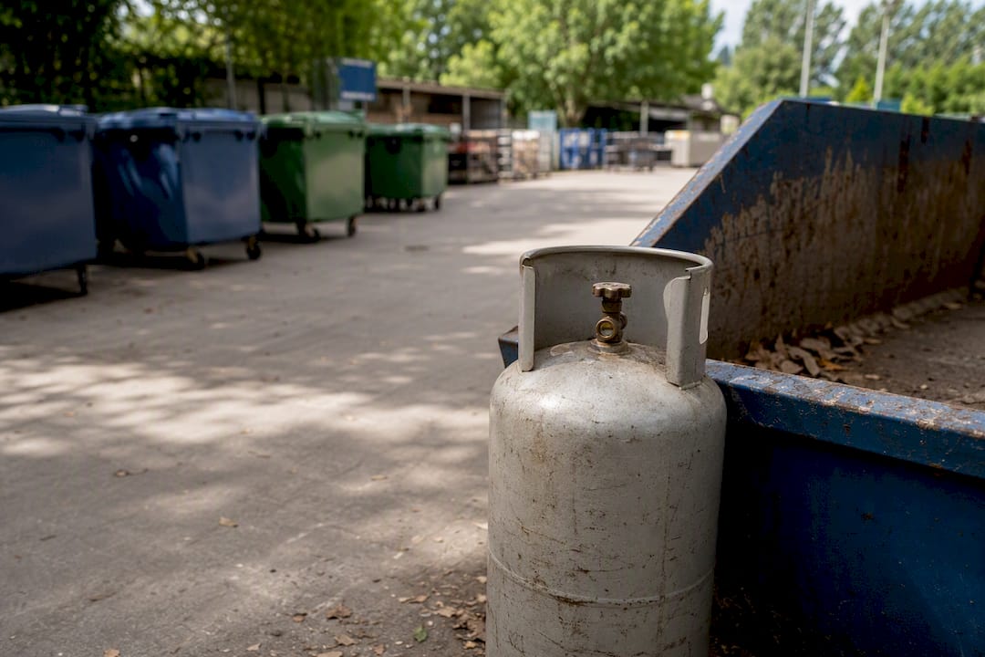 Close-up gas bottle next to skip bin